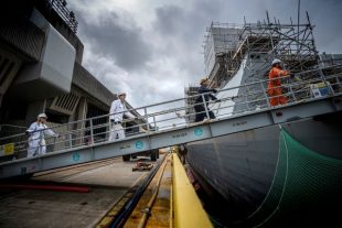 BAE employees walk up gangplank to naval ship with 2m distance between them