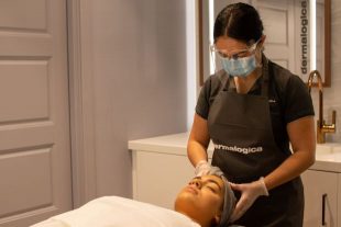 Beauty therapist wearing mask and visor giving client a facial